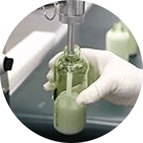 Hand holding a small glass bottle with a green liquid, with a blurred background