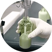 Hand holding a small glass bottle with a green liquid, with a blurred background