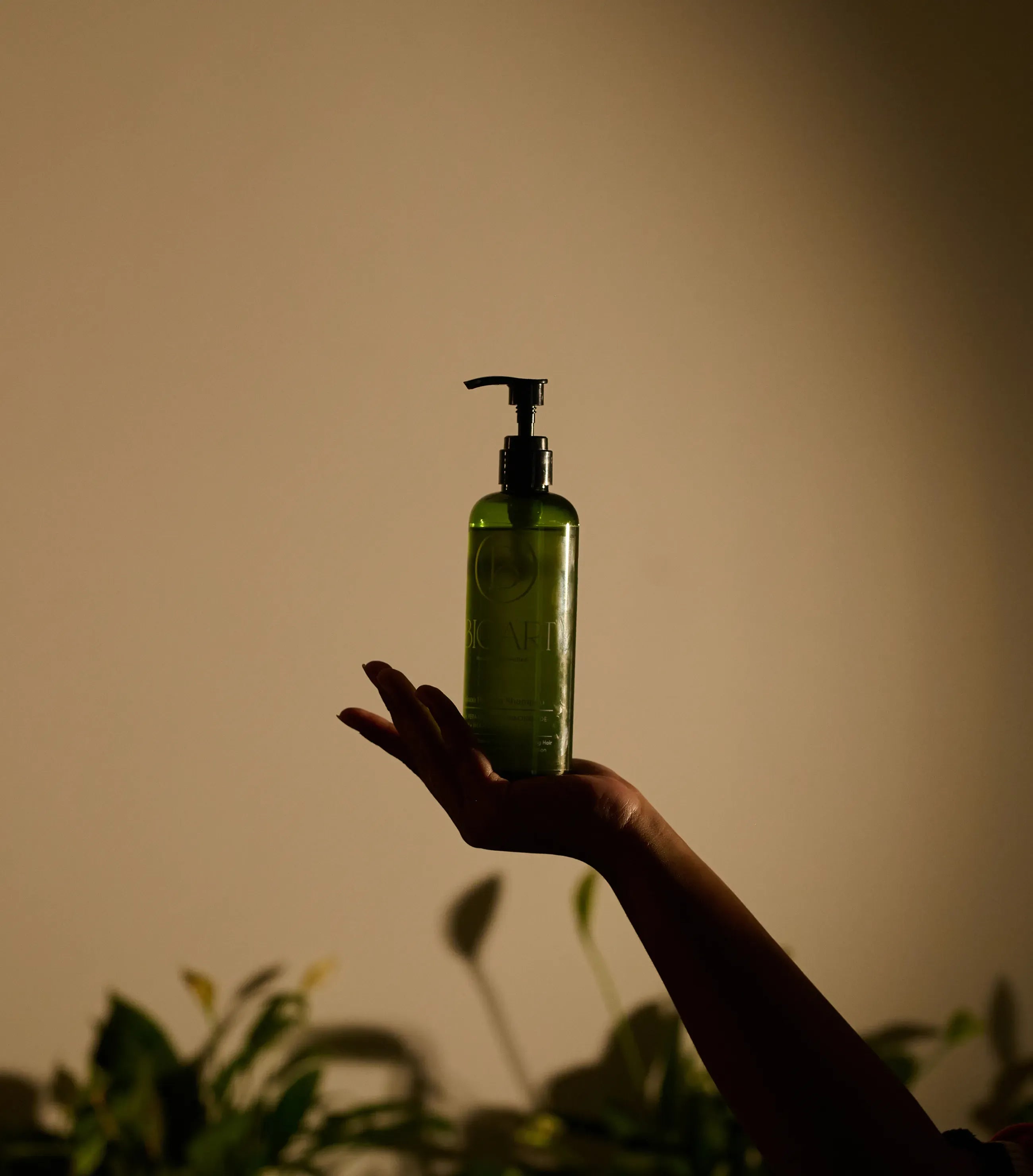 Hand holding a green bottle with pump against a beige background